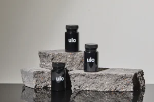 Black bottles of Ulo Rx solutions for thinning hair on a rock with a gray background